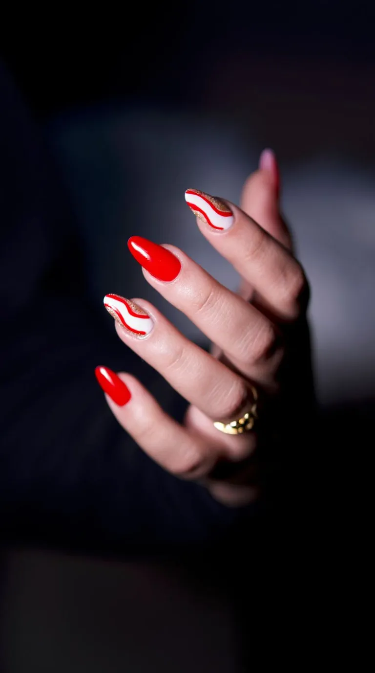 A close view of a hand with finished red and white nail art against a dark background