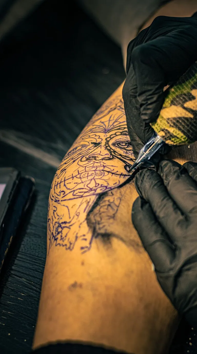 A tattoo machine working a detailed line drawing into a forearm in a studio, the artist in black gloves